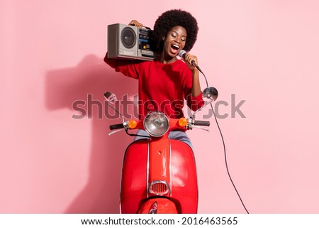 Portrait of attractive dreamy cheerful girl carrying player riding moped singing hit karaoke isolated over pink pastel color background