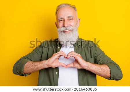 Photo portrait of senior man laughing showing heart shaped sign with hands isolated vibrant yellow color background