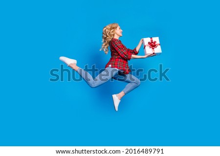 Photo of sweet charming lady wear plaid shirt smiling jumping holding present box looking empty space isolated blue color background