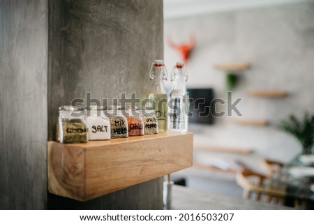 Close up picture of dried spices in glass jars on a wooden shelf in the kitchen. Spice jars in kitchen being displayed inline, paprika, pepper, spices, rosemary, basil, curry
