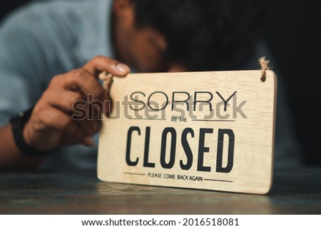 Business man holding a wooden sign with the message Shop closed due to coronavirus epidemic. Small SME bankruptcy concept.