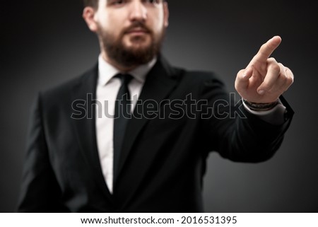 Close up in selective focus of businessman in suit, pointing index finger out, on black. Attention, augmented reality, virtual display, copy space concept