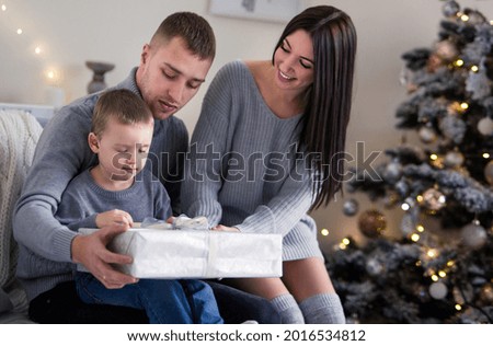 family - mom, dad and son in gray clothes open a Christmas present near the Christmas tree
