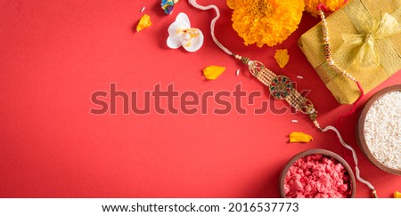 Raksha Bandhan, Indian festival with beautiful Rakhi and  Rice Grains on red background.  A traditional Indian wrist band which is a symbol of love between Sisters and Brothers. Royalty-Free Stock Photo #2016537773
