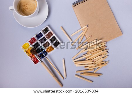 paints, colored pencils and a notebook are laid out on a gray background. Beautiful layout of the artist. High quality photo