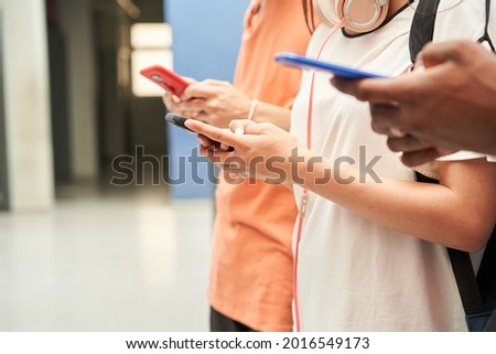 Close up of the hands of a multiethnic group of unrecognizable students using a smart phone. Connected, smiling people.