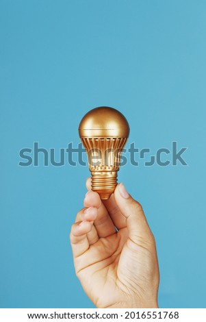 Gold light bulb as an idea in a female hand on a blue background. Isolate