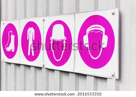 Posters with signs of safety of personal protective equipment in production in a row. Pink color on gray metal profile