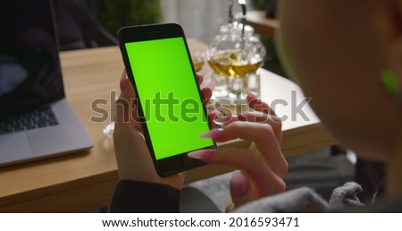 Close-up shooting. The girl is scrolling and pressing buttons on the phone with a chroma key. Green screen. The girl is sitting in a cafe and working. 4K