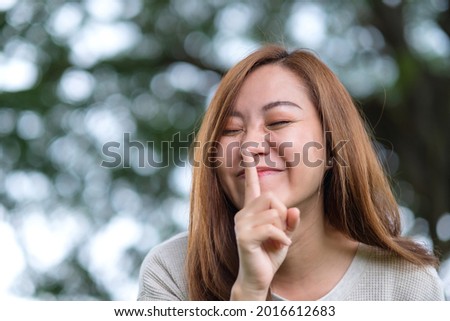 Portrait image of a young asian woman with index finger on lips, asking to be quiet or keep secret