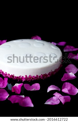 
Modern mousse cake with white mirror glaze in the shape of a round decorated with roses on a black background. Picture for a menu or a confectionery catalog. Vertical.