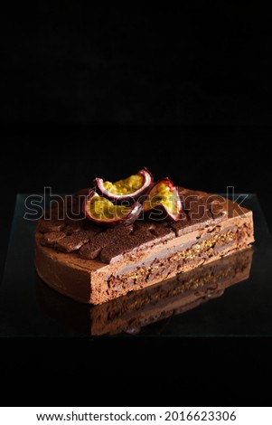 Delicious chocolate cake with passion fruit mousse decorated with chocolate ganache on a black background. Picture for a menu or a confectionery catalog. Vertical, text space. Layers, interior.
