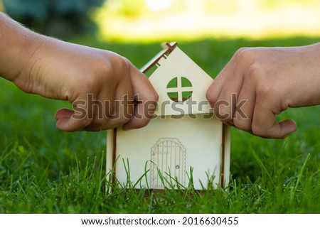 Kids collects a mock-up of a wooden house on the green grass. Close-up of hands. Family values. A house built by your own hands. Place for your text.