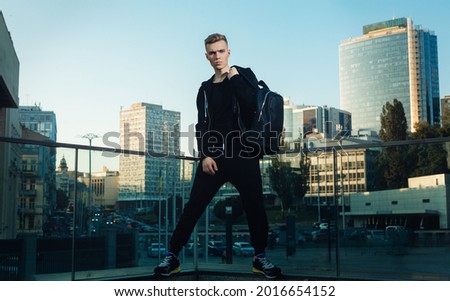 a young man with a backpack and in sportswear stands on the background of the city in the evening