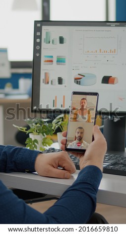 Disabled, invalid businessman in wheelchair discussing with friends on video call holding phone using headphones taking break sitting in business office. Diverse coworkers planning financial project