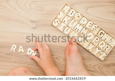 Wooden jigsaw letters of the alphabet from A to Z on natural wood floor. Learning to read. Toy for preschool Childs.  Kids hands on. Implement for nursery or kindergarten.  Boy writing his name.