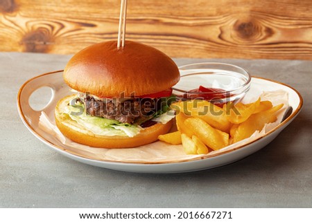 Fresh burger and potato wedges on gray wooden background