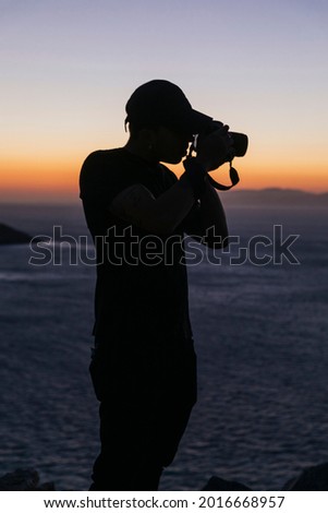Young man filmmaker at the top of a hill at sunset time
