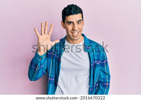 Handsome hispanic man wearing casual clothes showing and pointing up with fingers number five while smiling confident and happy. 