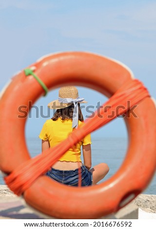 young skinny girl with straw hat and yellow t-shirt inside an orange plastic life buoy