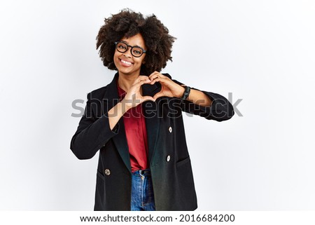 African american woman with afro hair wearing business jacket and glasses smiling in love doing heart symbol shape with hands. romantic concept. 