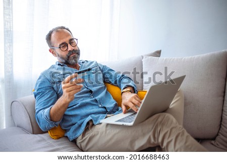 Modern mature man shopping online with credit card and laptop at home. Cropped shot of a mature man using a credit card to make an online payment at home