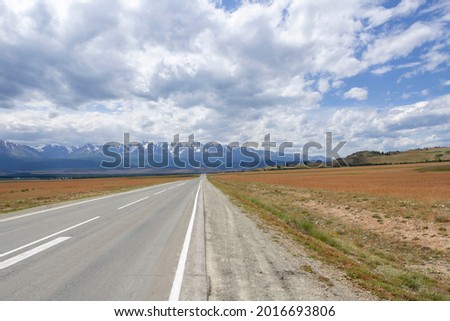 snowy peaks of mountains against the background of clouds and the road stretching into the distance