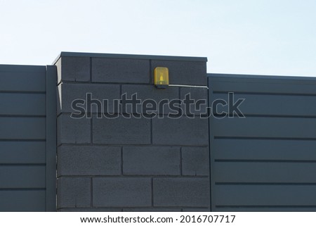 one yellow signal light hanging on a black brick wall of a fence on the street