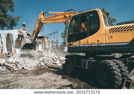 Destruction of old house by excavator. Bucket of excavator breaks concrete structure