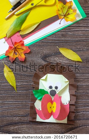 Autumn Greeting postcard hedgehog with an apple on a wooden table. Handmade. Project of children's creativity, handicrafts, crafts for kids.

