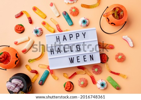 Halloween concept. Halloween party decorations with lightbox with words Happy Halloween, sweets, pumpkins top view flat lay on orange background
