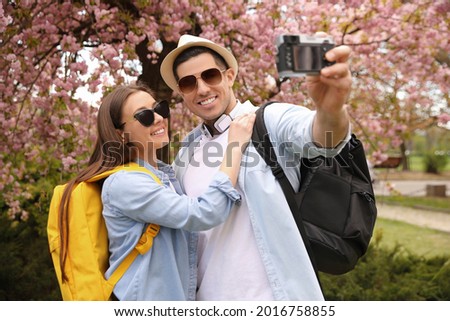 Happy couple of tourists taking selfie in blossoming park on spring day