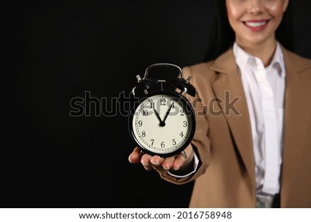 Businesswoman holding alarm clock on black background, closeup with space for text. Time management