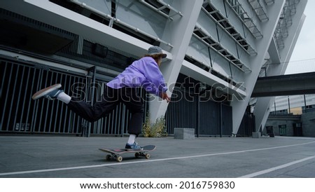 Young skater boy riding on skateboard in urban view. Active hipster practicing extreme ride on boardwalk in city stadium. Sporty skateboarder accelerating on skate board outdoors in slow motion.
