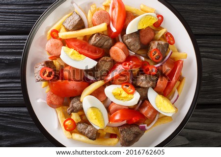 Bolivian Pique A Lo Macho is a dish prepared with cooked meat and sausage served over fries and garnished with vegetables, eggs closeup in the plate on the table. Horizontal top view from above Royalty-Free Stock Photo #2016762605
