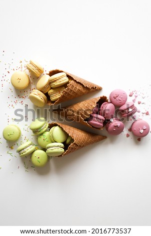 colourful french macarons pour out of the waffle cones like ice cream, yellow pink green cakes or cookies, healthy dessert with decor, white background, top view, close up, flat lay with copy space