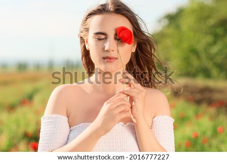 Beautiful young woman with poppy flower in field