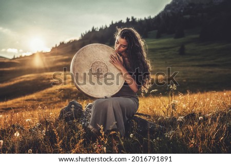 beautiful shamanic girl playing on shaman frame drum in the nature. Royalty-Free Stock Photo #2016791891