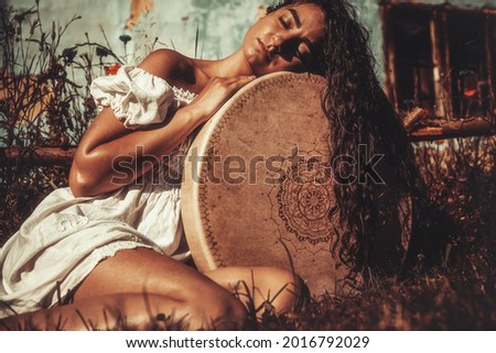 beautiful shamanic girl playing on shaman frame drum in the nature. Royalty-Free Stock Photo #2016792029