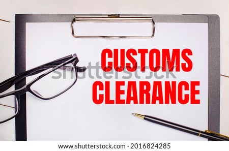 On a light wooden background glasses, a pen and a sheet of paper with the text CUSTOMS CLEARANCE. Business concept