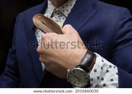 a large bundle of money in the hand of a man in an expensive suit, a watch on his hand, making money.