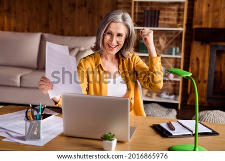 Photo of charming lucky woman dressed yellow shirt spectacles working modern gadget holding documets indoors workshop workplace