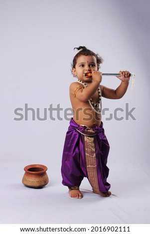 adorable Indian baby in krishna kanha or kanhaiya dress posing with his flute and peacock feather on white background. standing pose