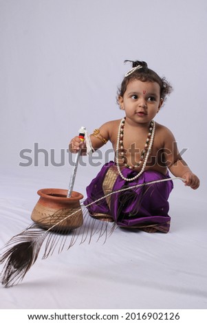 adorable Indian baby in krishna kanha or kanhaiya dress posing with his flute and peacock feather on white background. standing pose