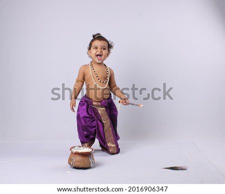 Janmashtami concept- adorable Indian baby in krishna kanha or kanhaiya dress posing with his flute and dahi handi (pot with curd) on white background. standing pose