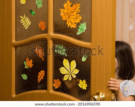 child girl decorates the door in the room with paper pictures of autumn leaves. maple, rowan, birch colored paper decorations.