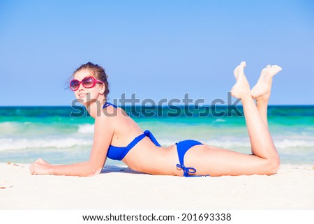 young woman in bikini lying on white sand beach