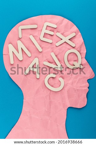 Head silhouette made of paper and white wooden letters. Crumpled pink paper shaped as a human head with copy space on blue paper background. Mind and thinking concept.