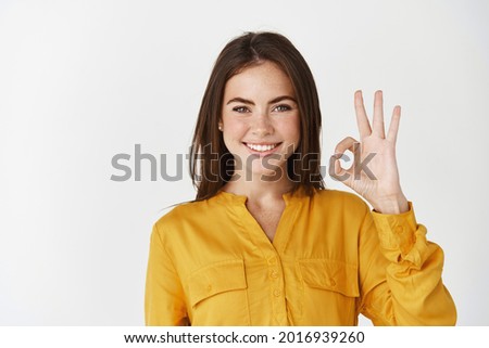 Young confident woman smiling, showing okay gesture, saying yes or alright and standing on white background