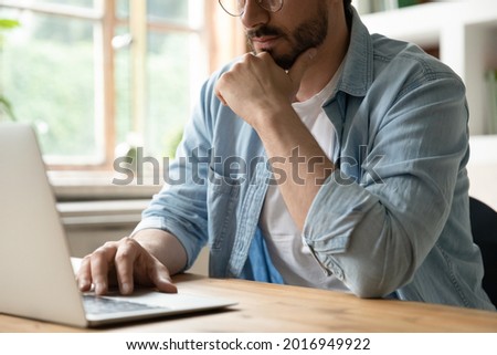 Cropped image thoughtful young man working on computer, sitting at table. Pensive millennial male manager worker employee analyzing electronic documents, considering problem solution, communicating.